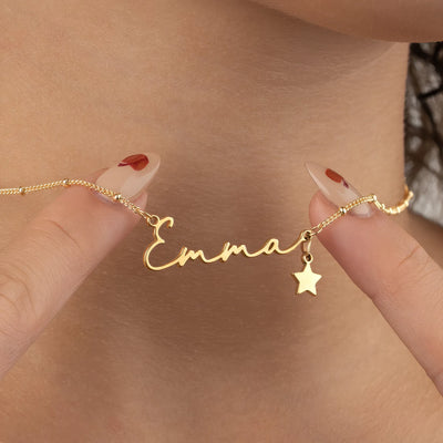 Close-up of a polished yellow gold cursive Emma name necklace with a star charm and bead chain, held against the neck