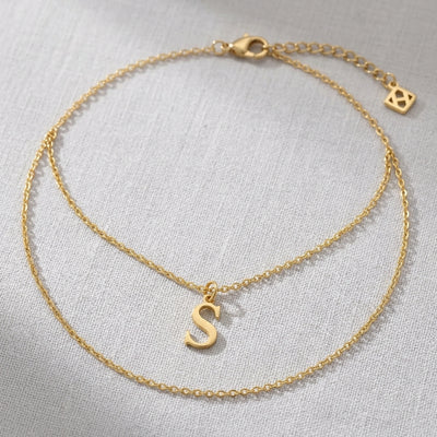 Personalised 18ct gold initial necklace with the letter S in the Bella style, laid flat on linen, showing the whole necklace.