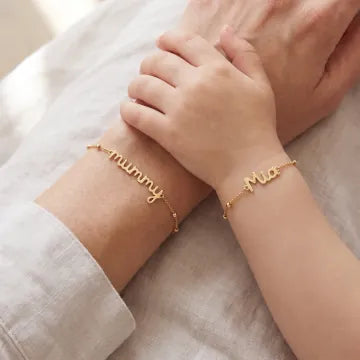 A mother and child wearing matching gold handwriting bracelets, wrists side by side