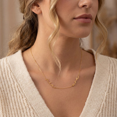 Close-up of a woman wearing a gold double name necklace with a neutral background